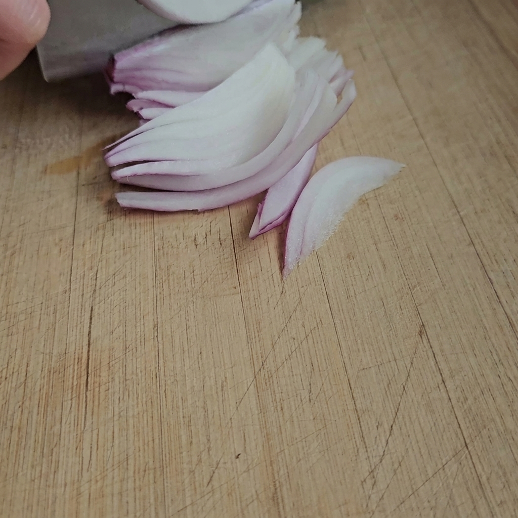 Sottili fette di zenzero fresco pronte su un tagliere di legno.