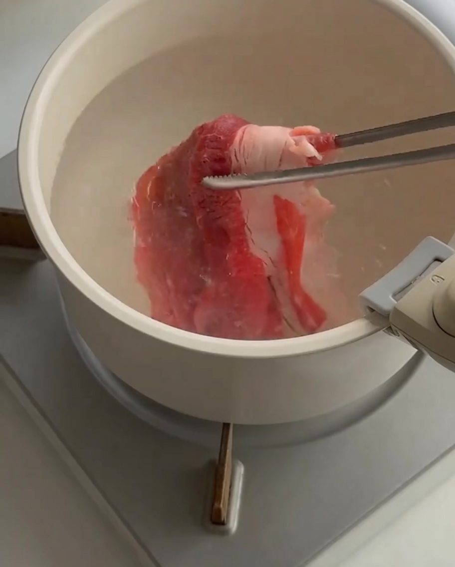 Fette sottili di manzo crudo immerse in una pentola di acqua bollente con le pinze.