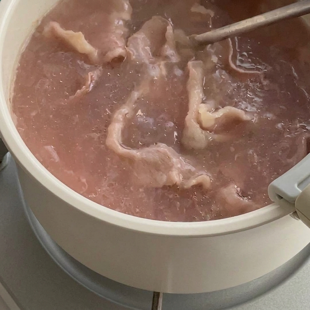 Fette di manzo che cambiano colore in acqua bollente, sollevate con un colino.