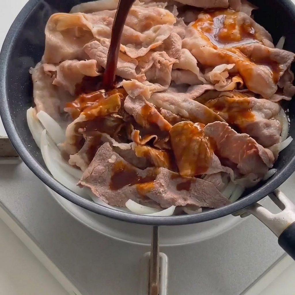 Salsa scura versata sul manzo e le cipolle in una padella calda.