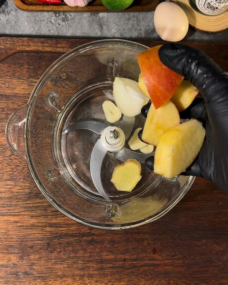 Un contenitore da frullatore riempito con mela, cipolla, aglio, zenzero e acqua.