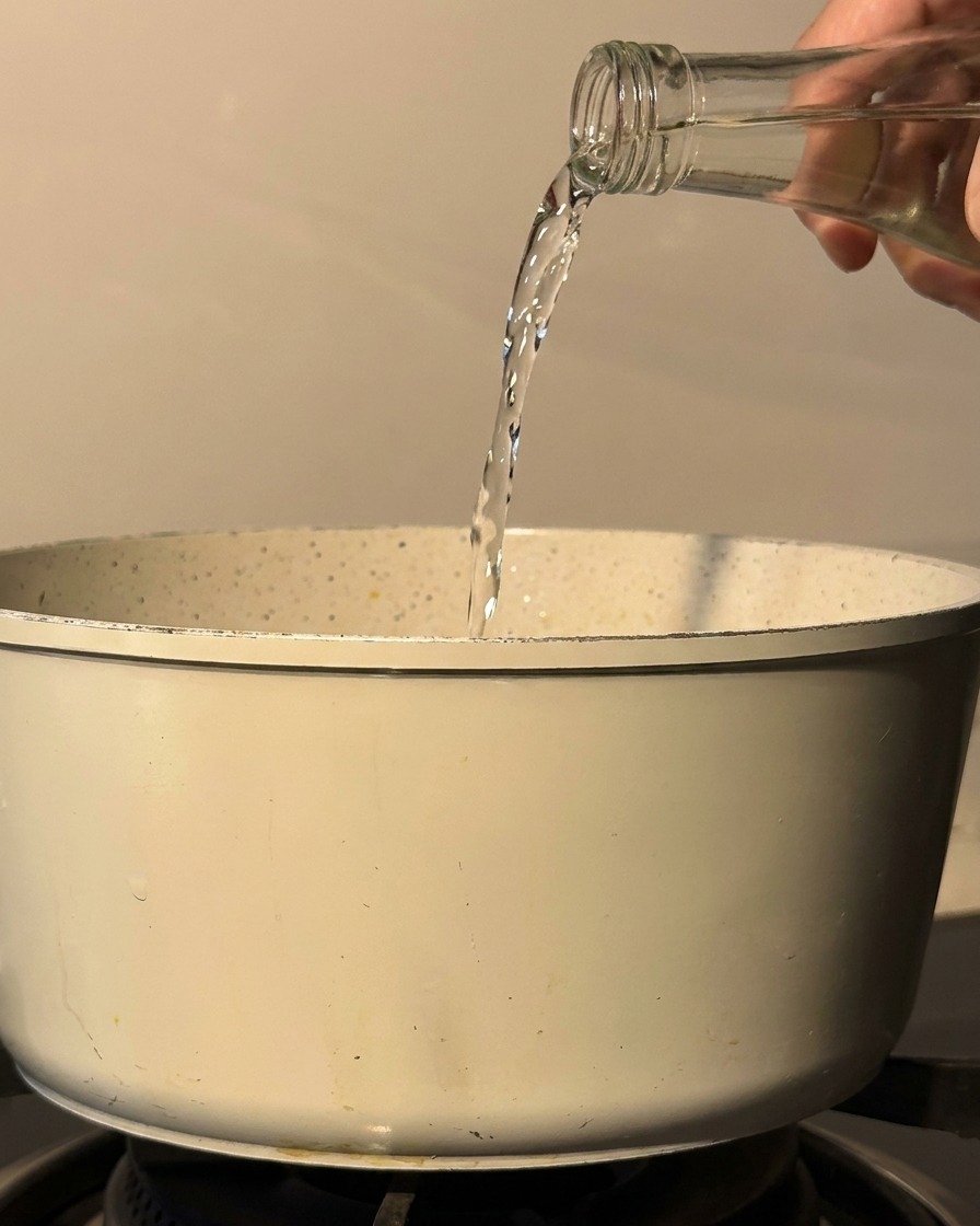 Sake e mirin versati da una bottiglia di vetro in una pentola su un piano cottura.