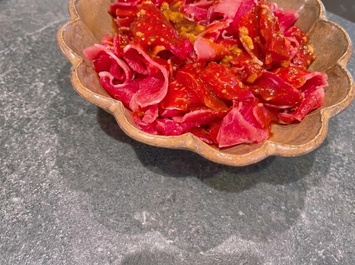 Sottili fette di manzo crudo ricoperte da una scura marinata al miso allinterno di un piatto smerlato marrone.