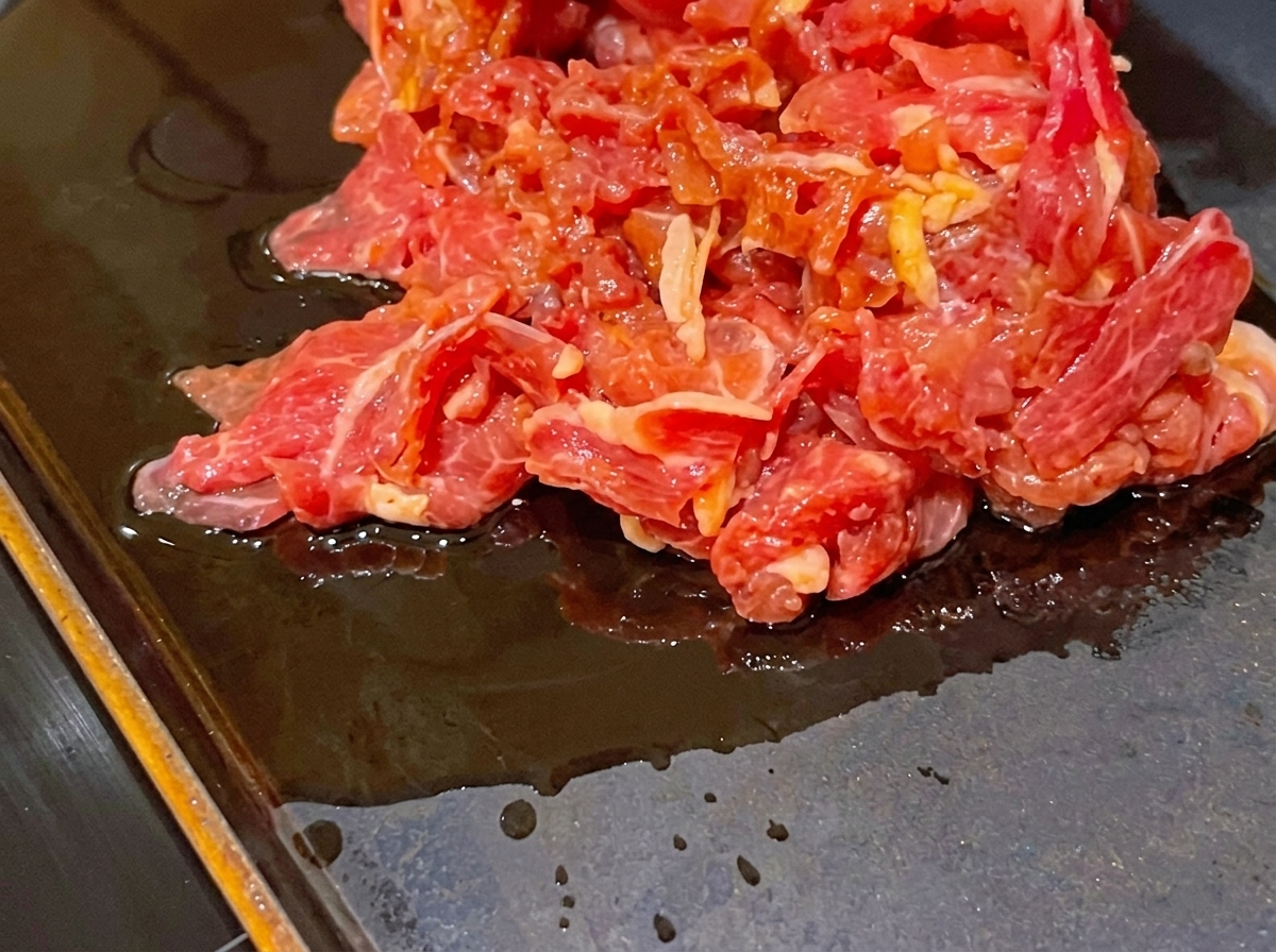 Un mucchio di fette di manzo crudo marinato su una padella piatta, scura e calda.