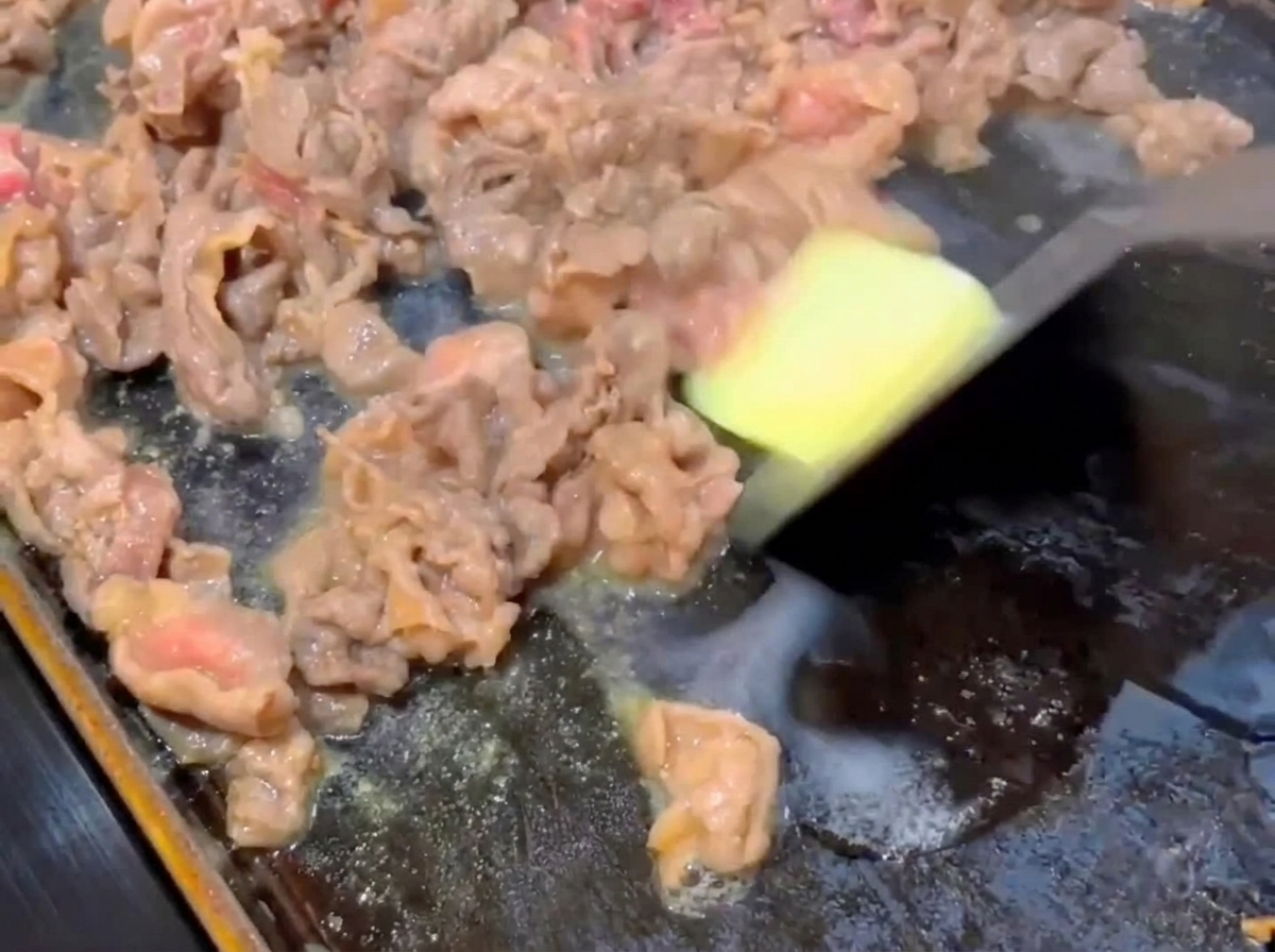 Un piccolo cubetto di burro che si scioglie su fette di manzo parzialmente cotte in una padella piatta calda.