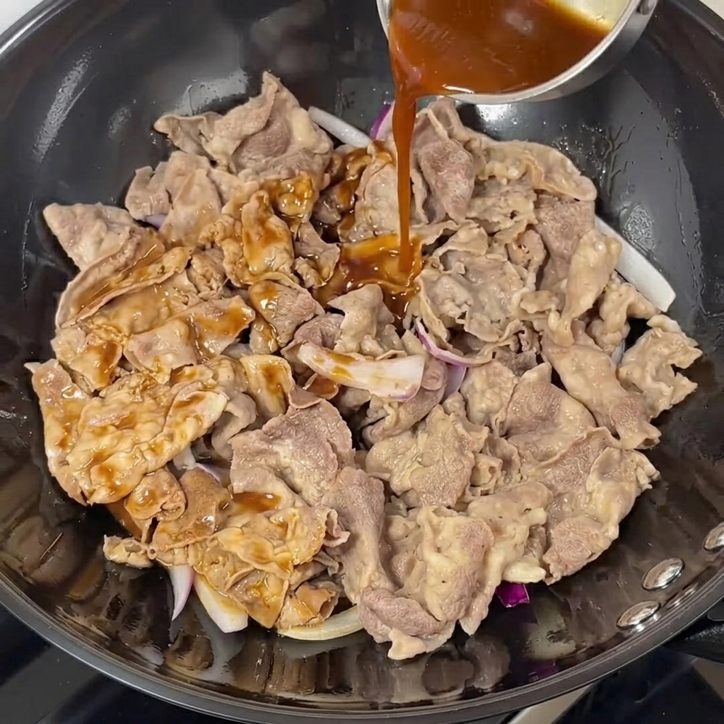 Salsa teriyaki scura versata su manzo e cipolle nel wok.