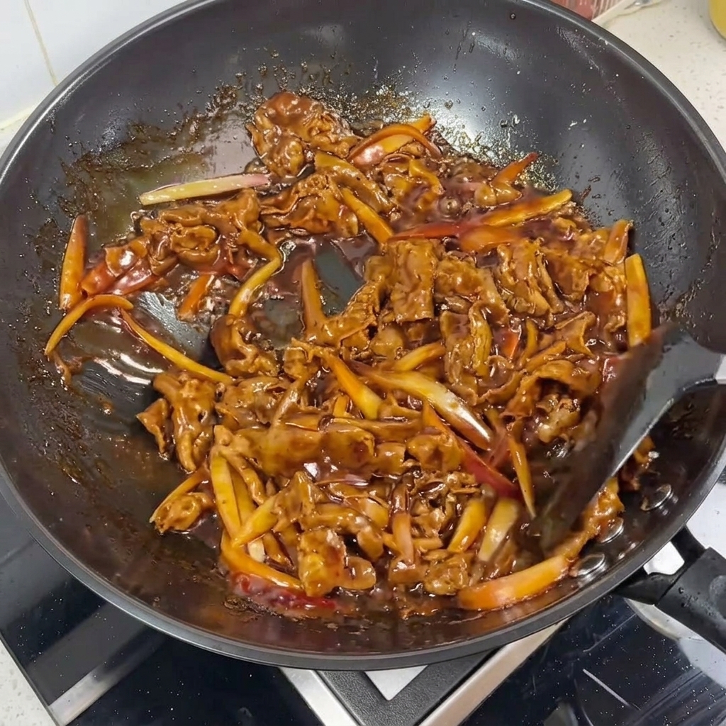 Primo piano di straccetti di manzo e cipolle glassati in una salsa teriyaki lucida e scura.