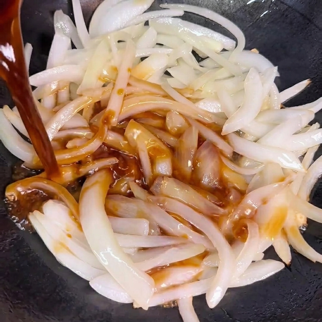 Salsa versata sopra le cipolle saltate in un wok.
