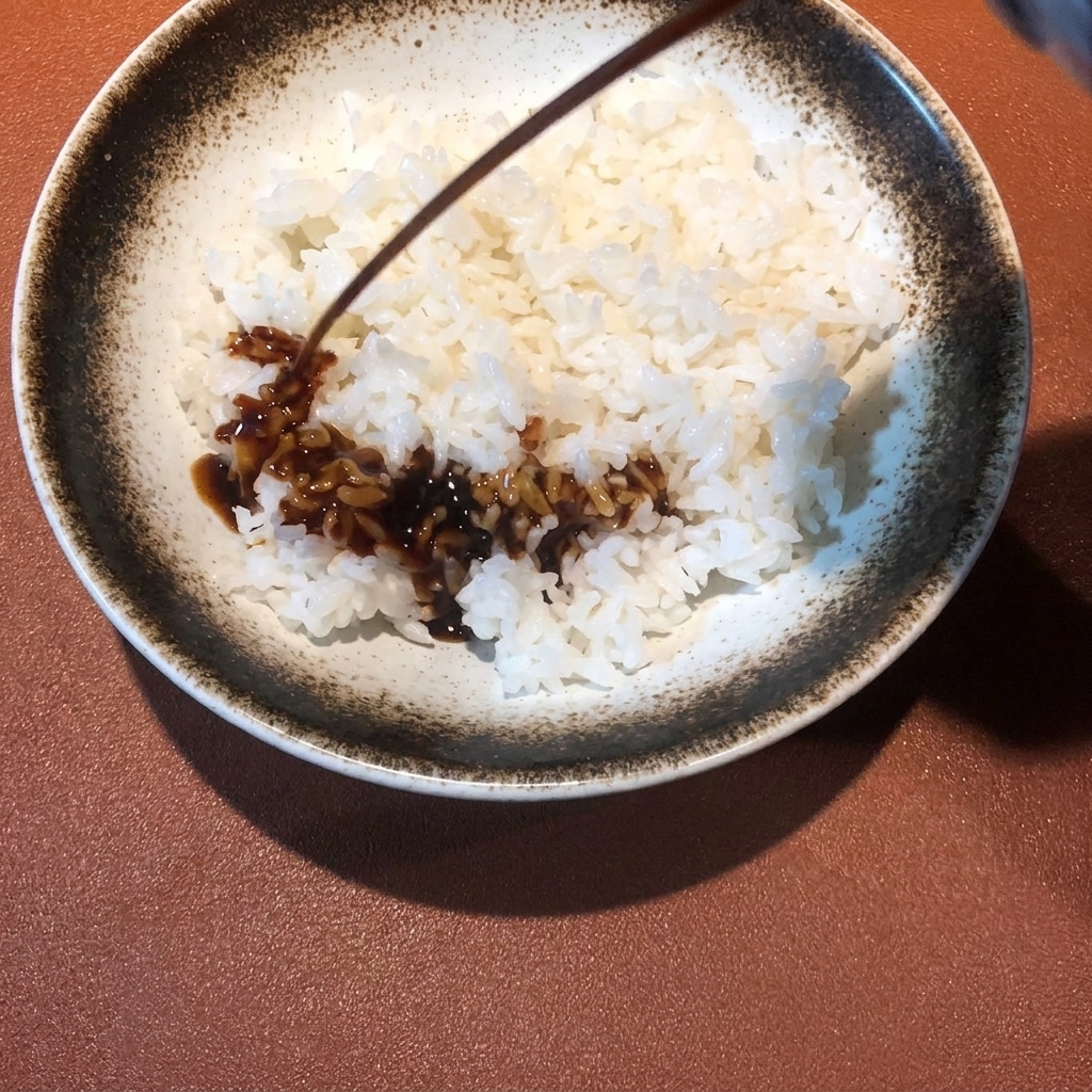 Salsa ricca e scura che viene versata dallalto su una ciotola di riso bianco fumante.