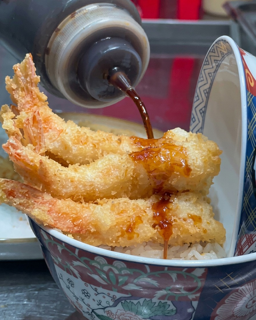 Salsa scura versata a filo sui gamberi fritti.