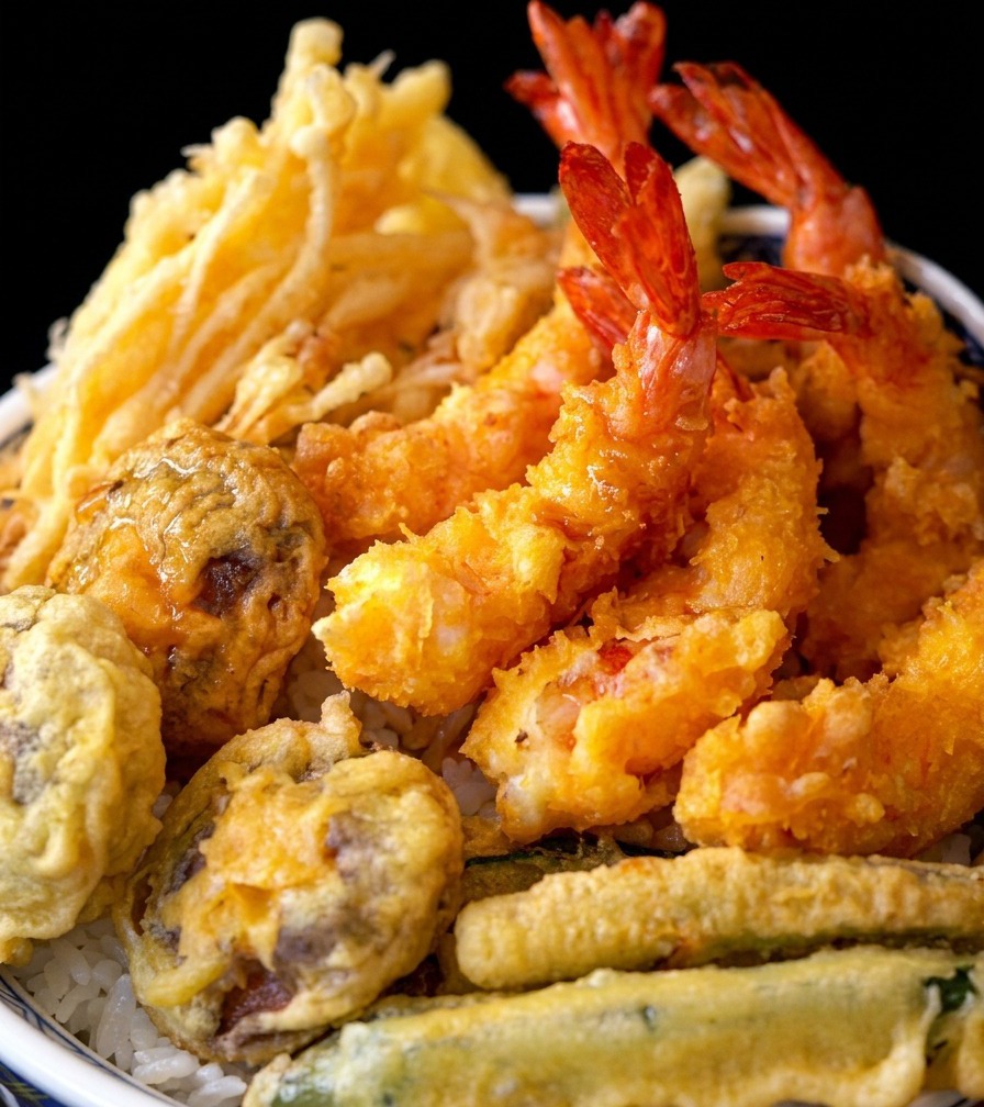 Una ciotola di riso con tempura finita guarnita con gamberi e verdure fritte croccanti.