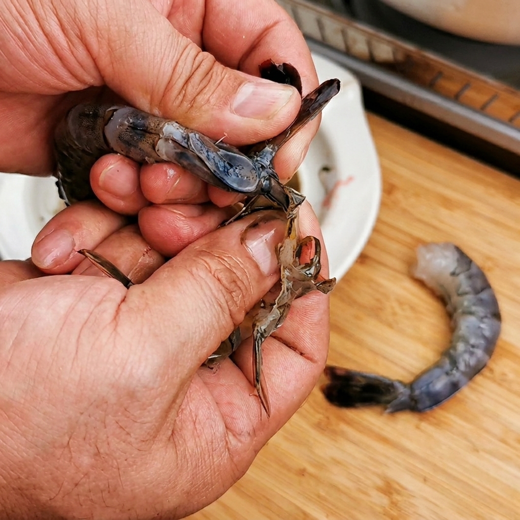 Primo piano di mani che puliscono un gambero crudo mantenendo la coda attaccata.