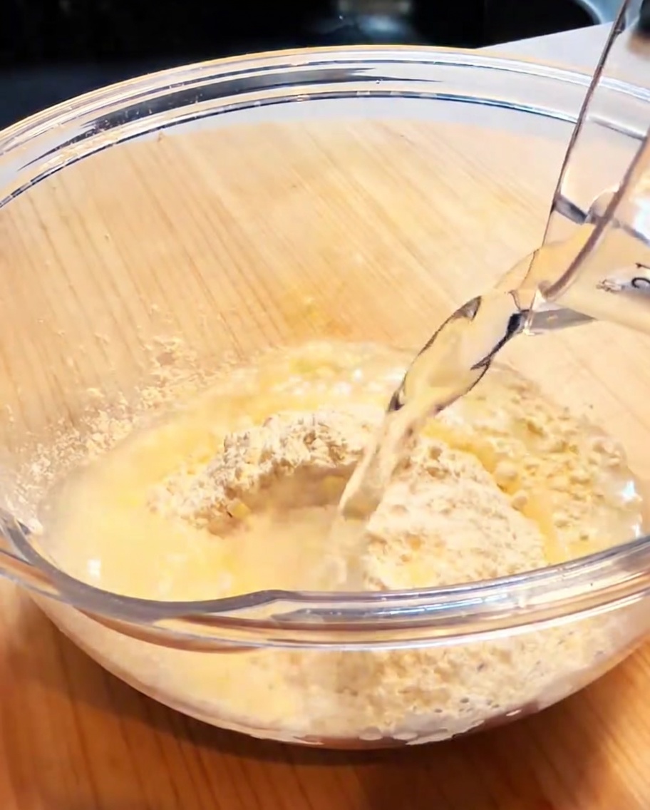 Una ciotola di vetro contenente farina per tempura e acqua, mescolata per formare una pastella liscia e leggera.