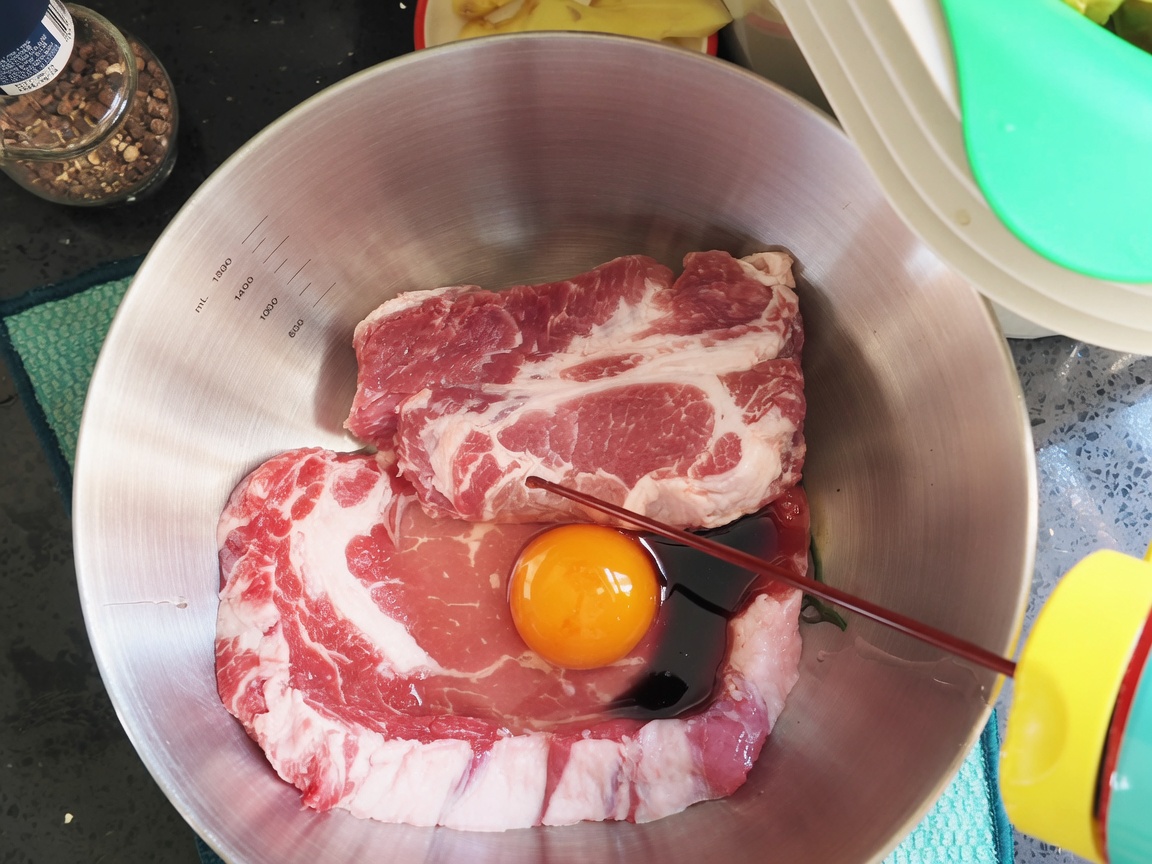 Salsa di soia scura e condimenti versati sopra le braciole di maiale e luovo in una ciotola.