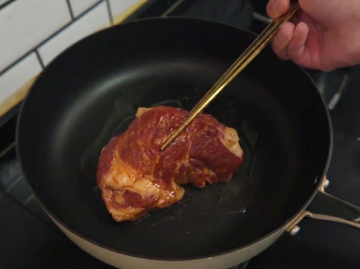 Una braciola di maiale marinata cruda che viene adagiata in una padella calda con olio di semi.