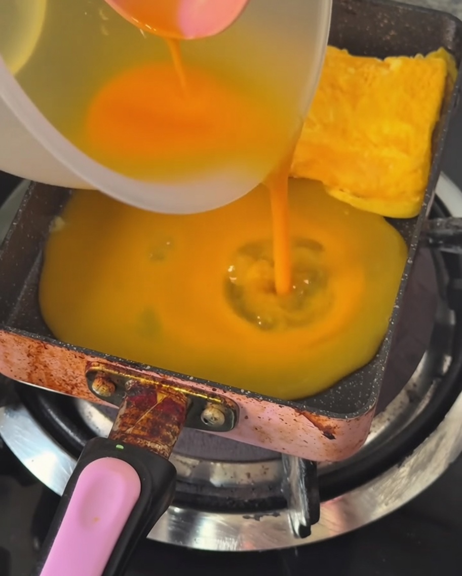 Un sottile strato di uovo sbattuto versato in una padella rettangolare calda e unta.