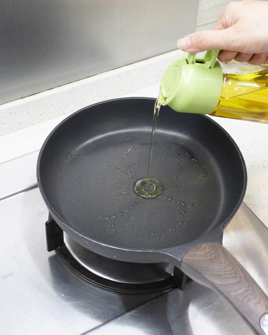 Una vista ravvicinata di olio versato in una padella antiaderente preriscaldata, pronta per languilla.