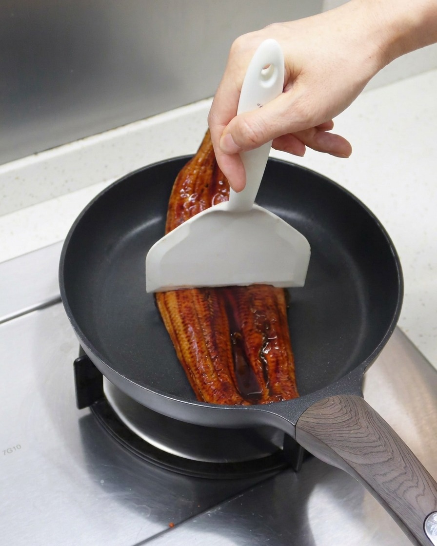 Languilla grigliata divisa in due pezzi con una spatola bianca allinterno di una padella.