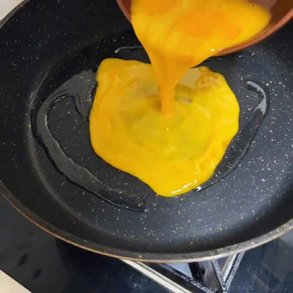Uova sbattute versate in una padella calda dal fondo scuro.