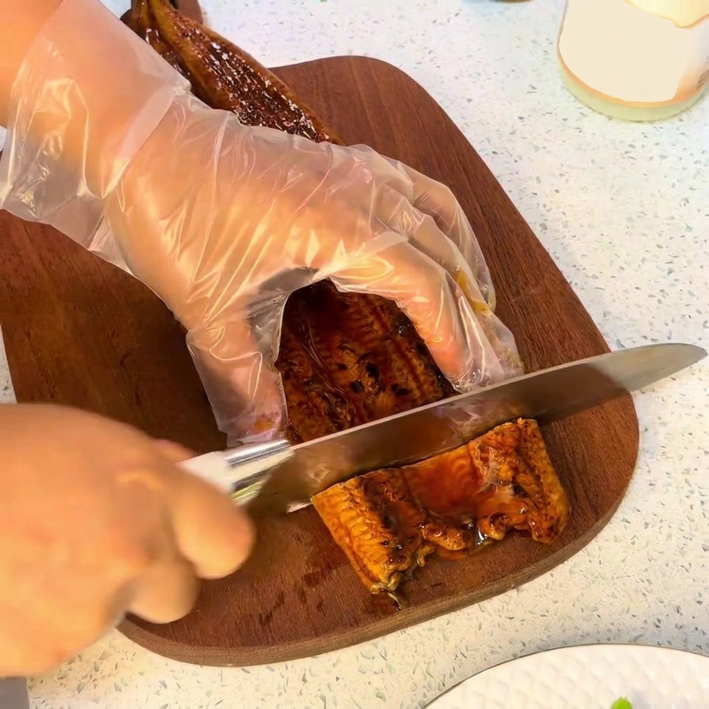 Un coltello taglia un pezzo di anguilla grigliata su un tagliere di legno.