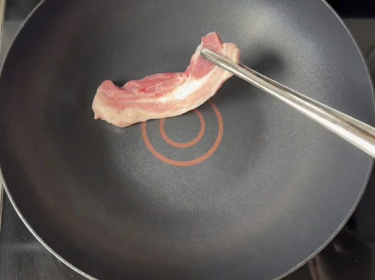 Fette di pancetta dorate che friggono in una padella antiaderente asciutta.
