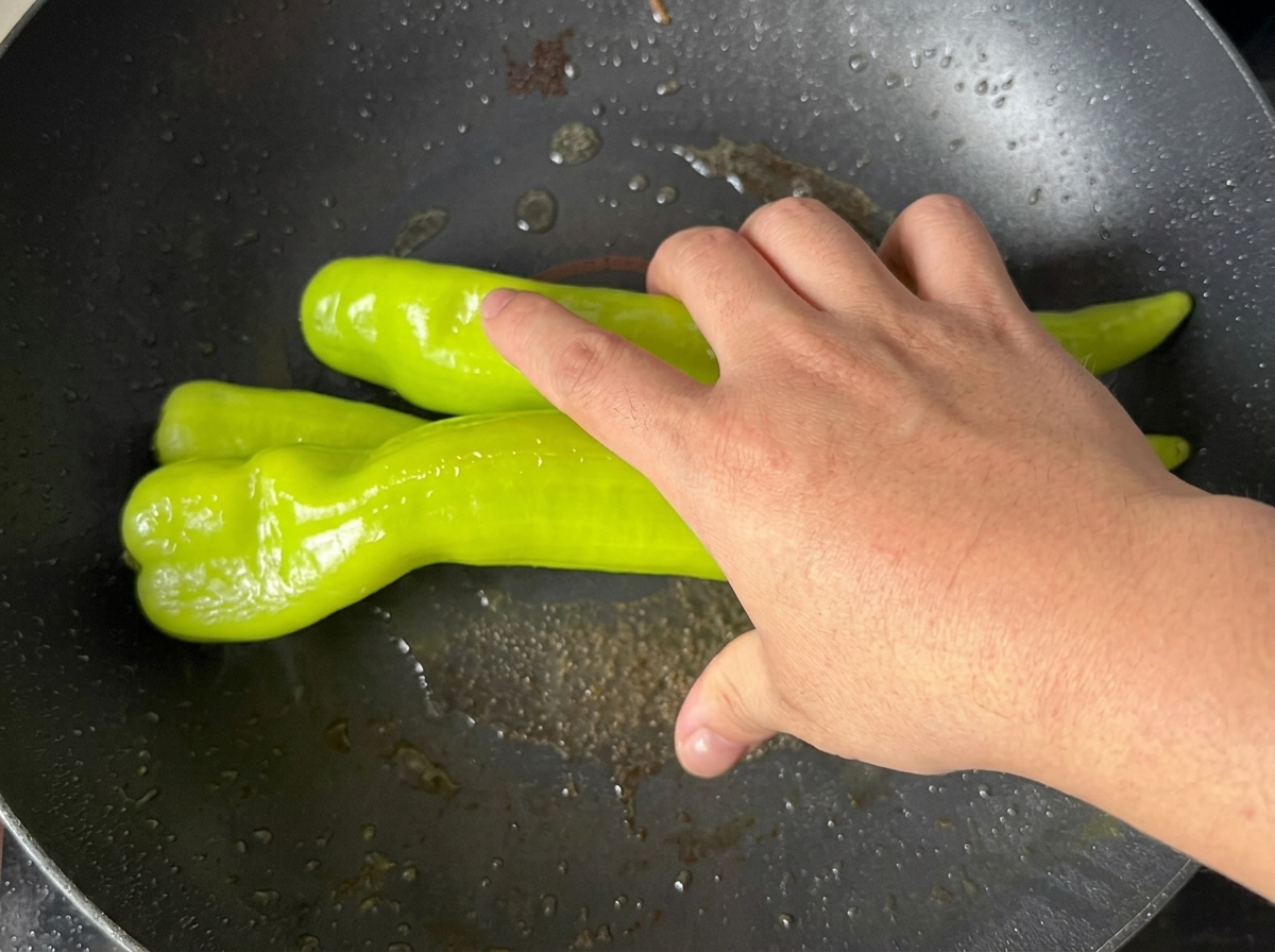 Peperoni verdi che friggono in padella finché la pelle non diventa bruciacchiata.