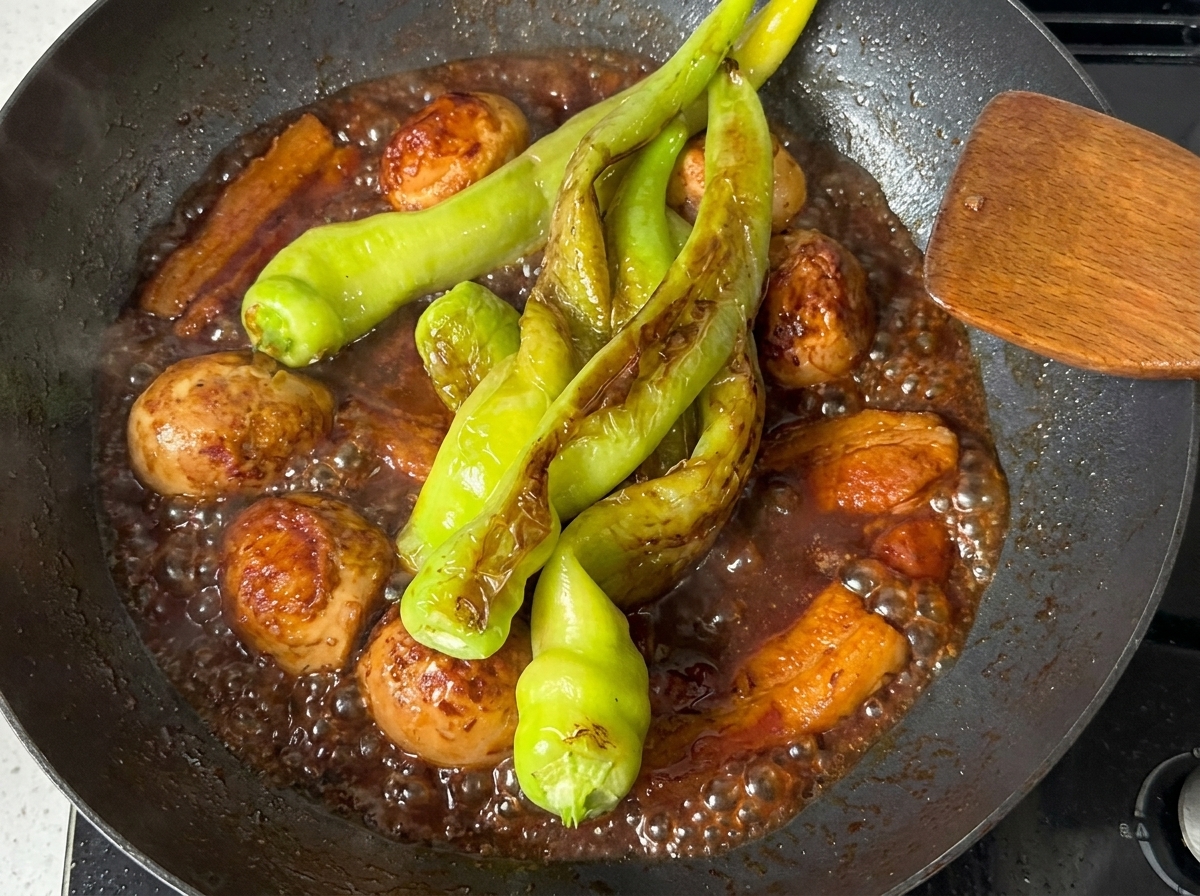 Peperoni verdi che sobbollono nel sugo ricco e scuro con pancetta e uova sode in padella.