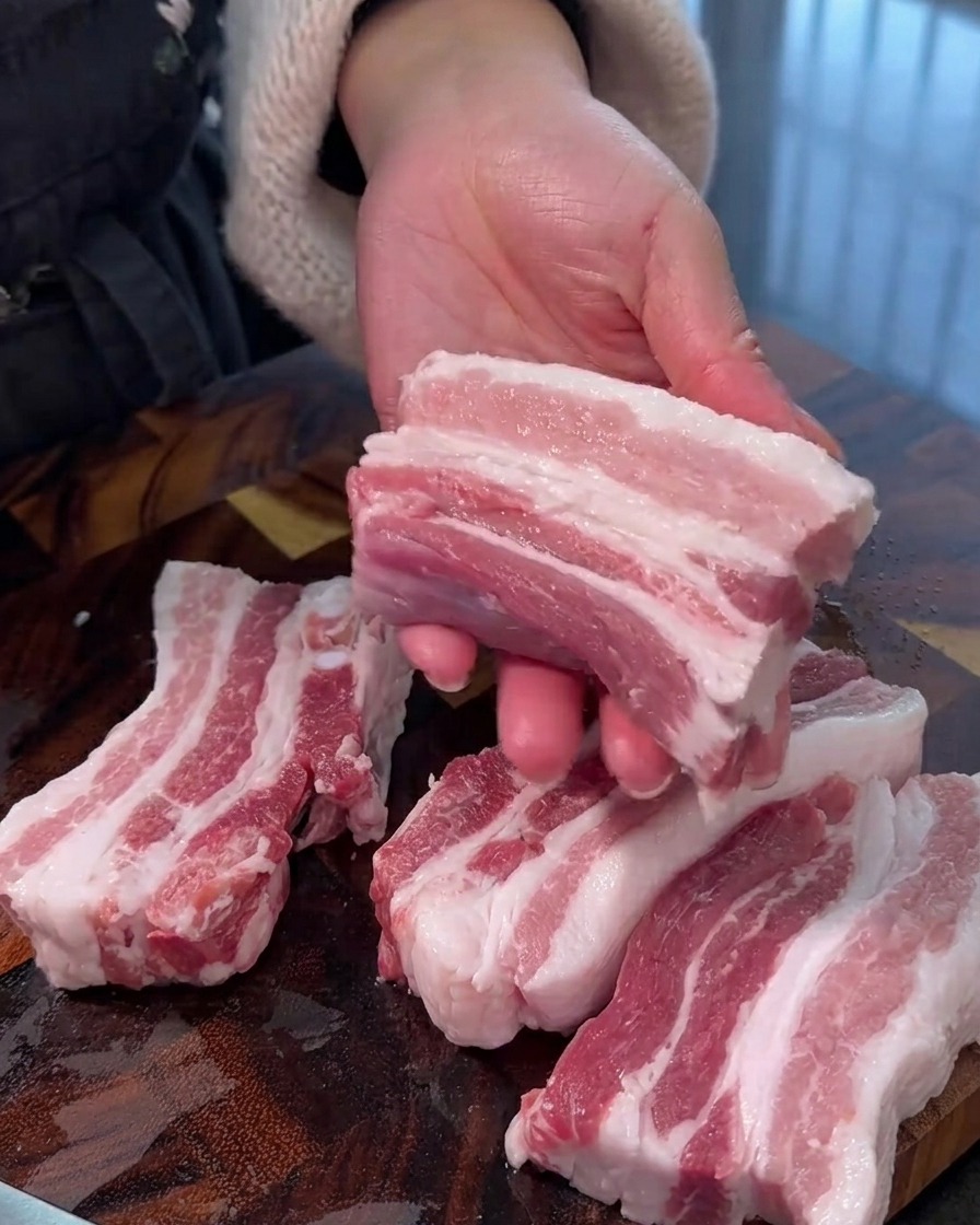 Pancetta cruda tagliata in strisce uniformi su un tagliere di legno.