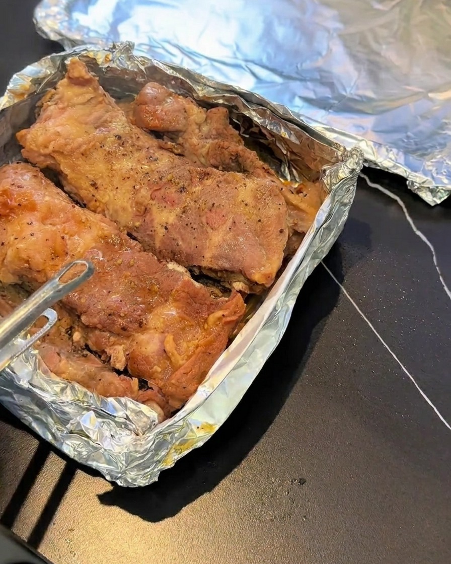 Costine cotte al vapore su una teglia foderata di alluminio e condite con pepe nero.
