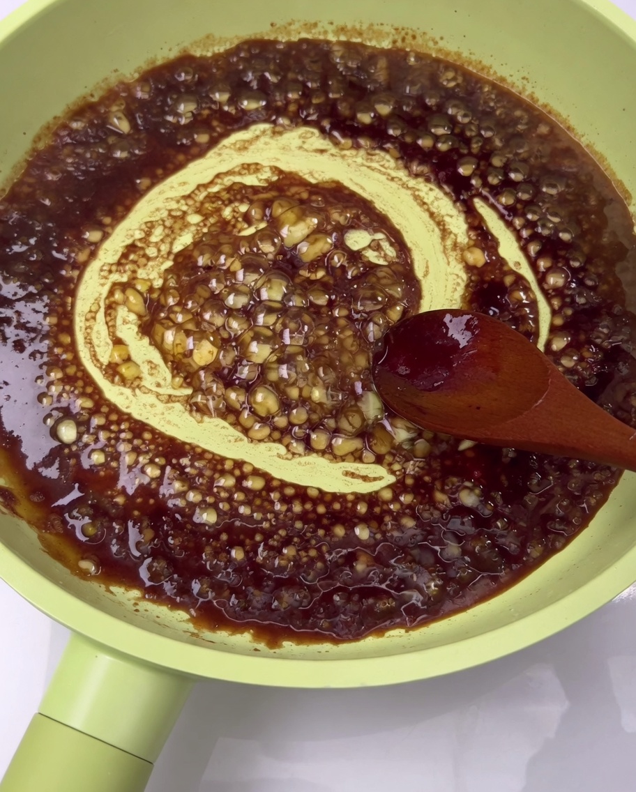 Costine di maiale cotte ricoperte da una salsa ricca e scura allinterno di una padella.