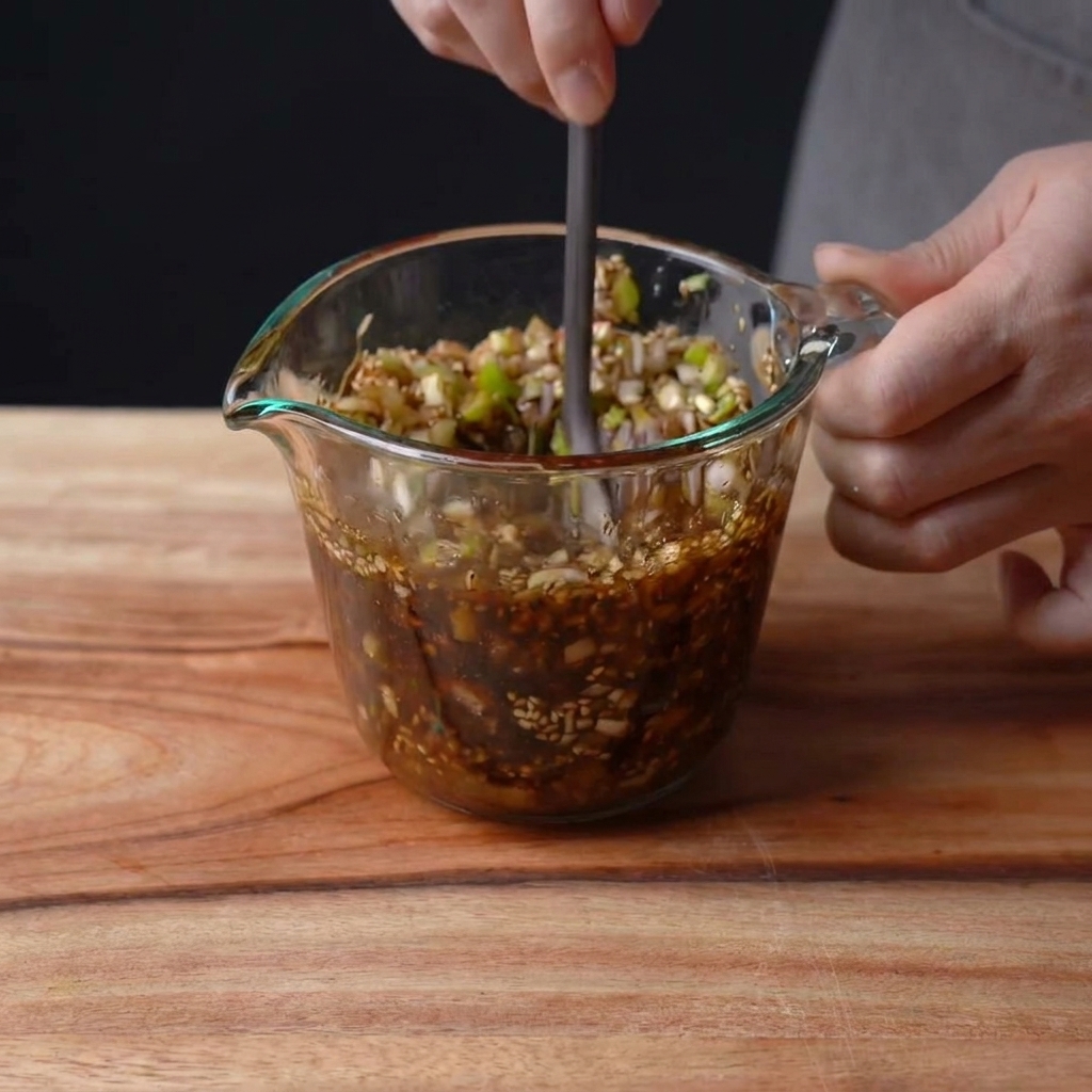 Una mano che mescola una salsa scura e ricca in un misurino di vetro.