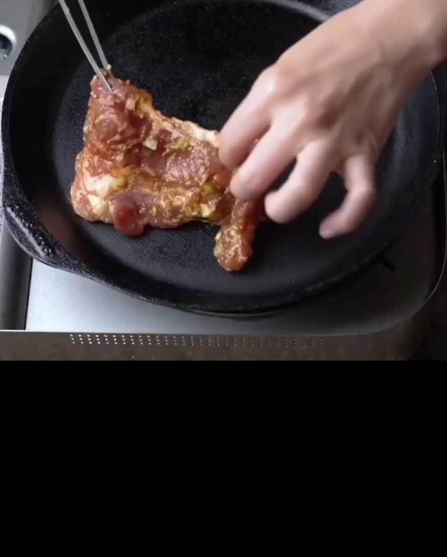 Costine di maiale marinate che sfrigolano in una padella di ghisa calda.