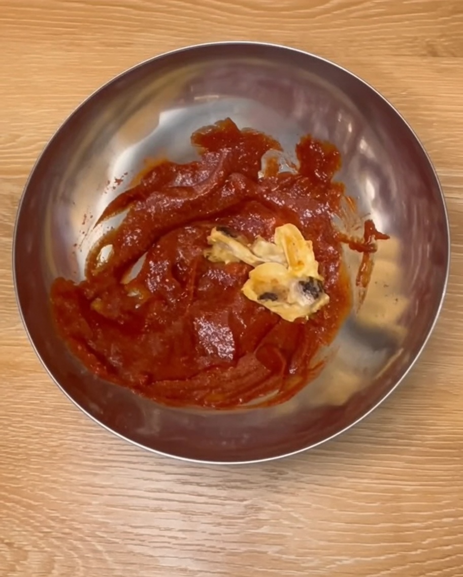 Cosce di pollo cotte mescolate con una ricca salsa rossa in stile coreano in una ciotola dacciaio.