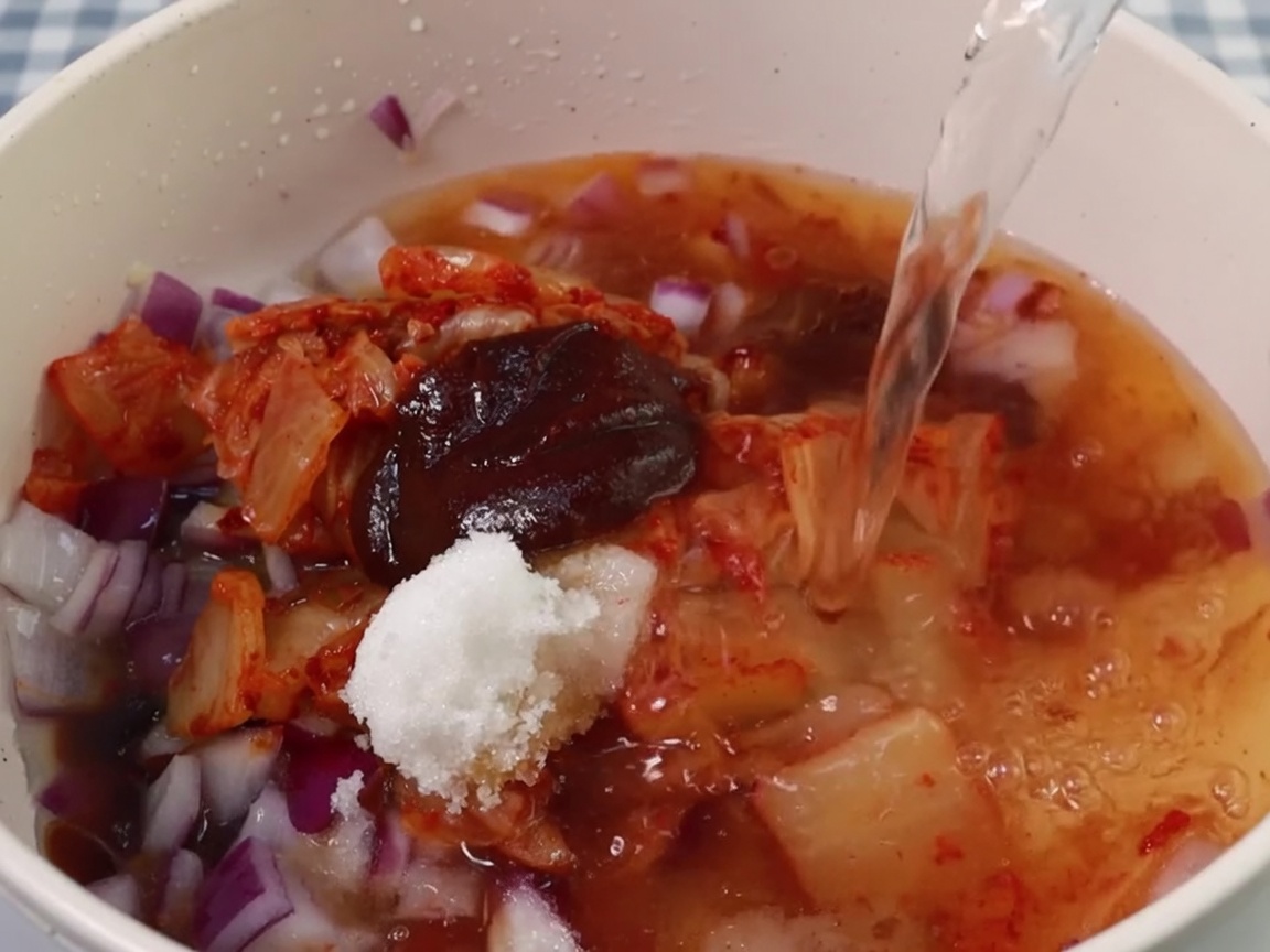 Acqua versata nella pentola con la base di kimchi e condimenti.