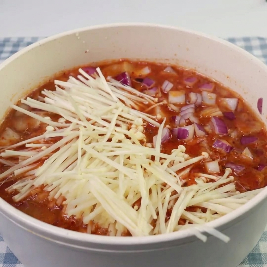 Funghi enoki e pezzi di spam aggiunti alla zuppa di kimchi in ebollizione.