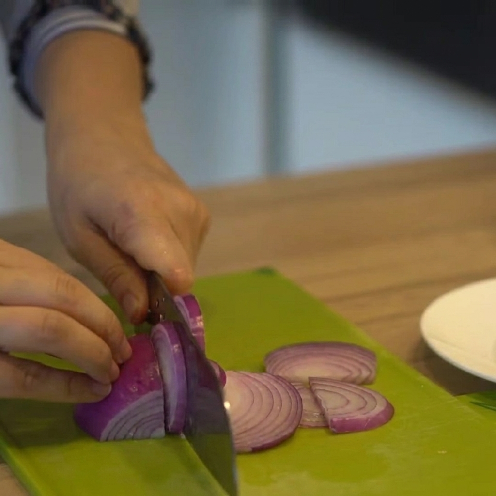 Cipolla rossa tagliata a fettine sottili su un tagliere verde.