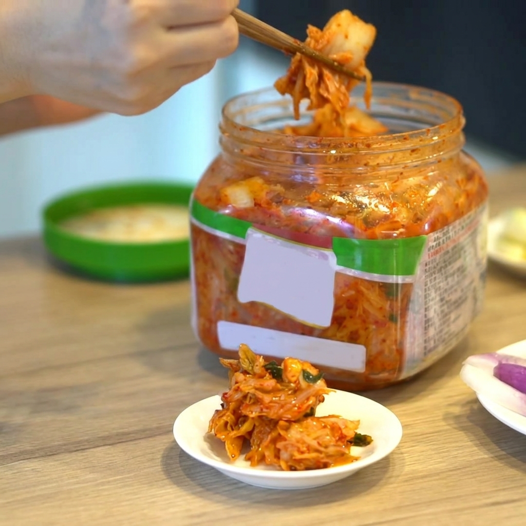 Una porzione di kimchi coreano prelevata da un contenitore con le bacchette.