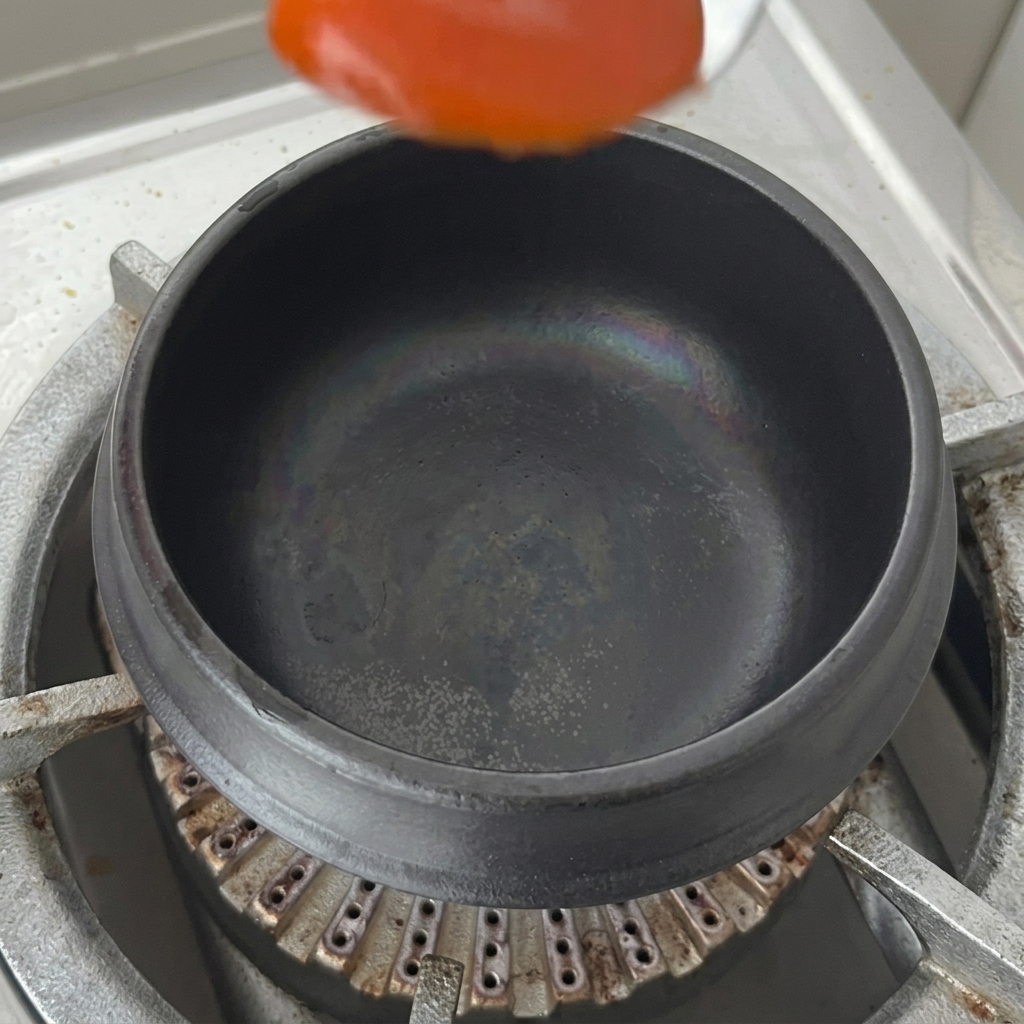 Un cucchiaio di salsa piccante al peperoncino messo sul fondo di una pentola di terracotta asciutta sui fornelli.