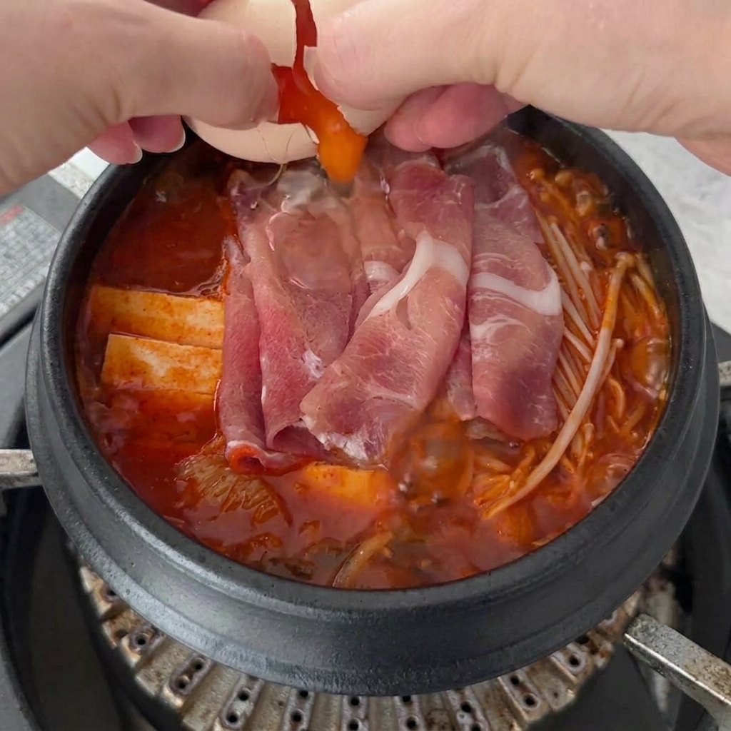 Due uova fresche rotte sulla superficie bollente del Kimchi Jjigae.