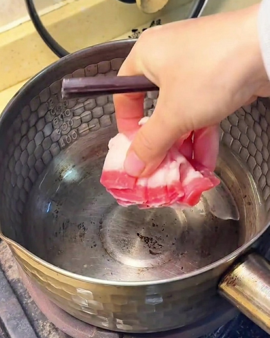 Fette di pancetta che friggono in una pentola dacciaio, con il grasso sciolto visibile sul fondo.