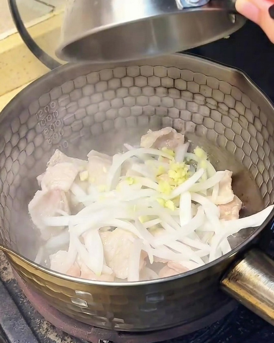 Fette di cipolla e aglio tritato che vengono aggiunti nella pentola con la pancetta cotta.