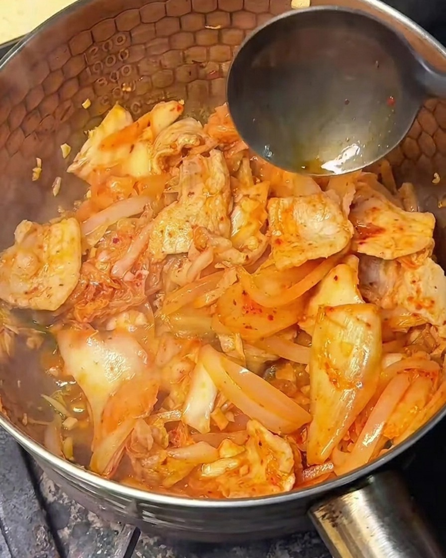 Salsa di soia chiara versata nel composto di kimchi e pancetta saltato.