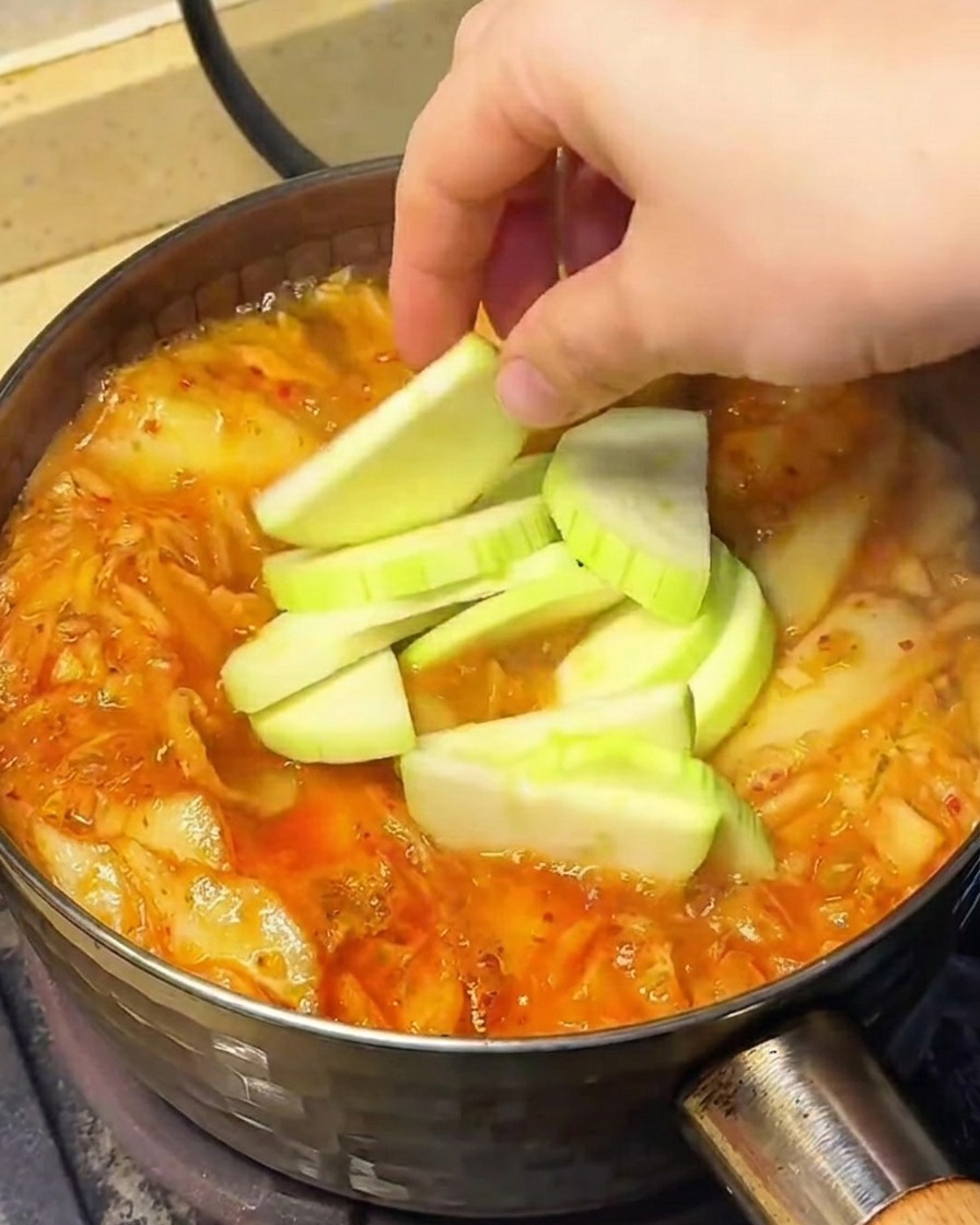 Verdure, tra cui fette di chayote, germogli di soia e funghi enoki, aggiunte alla zuppa che sobbolle.