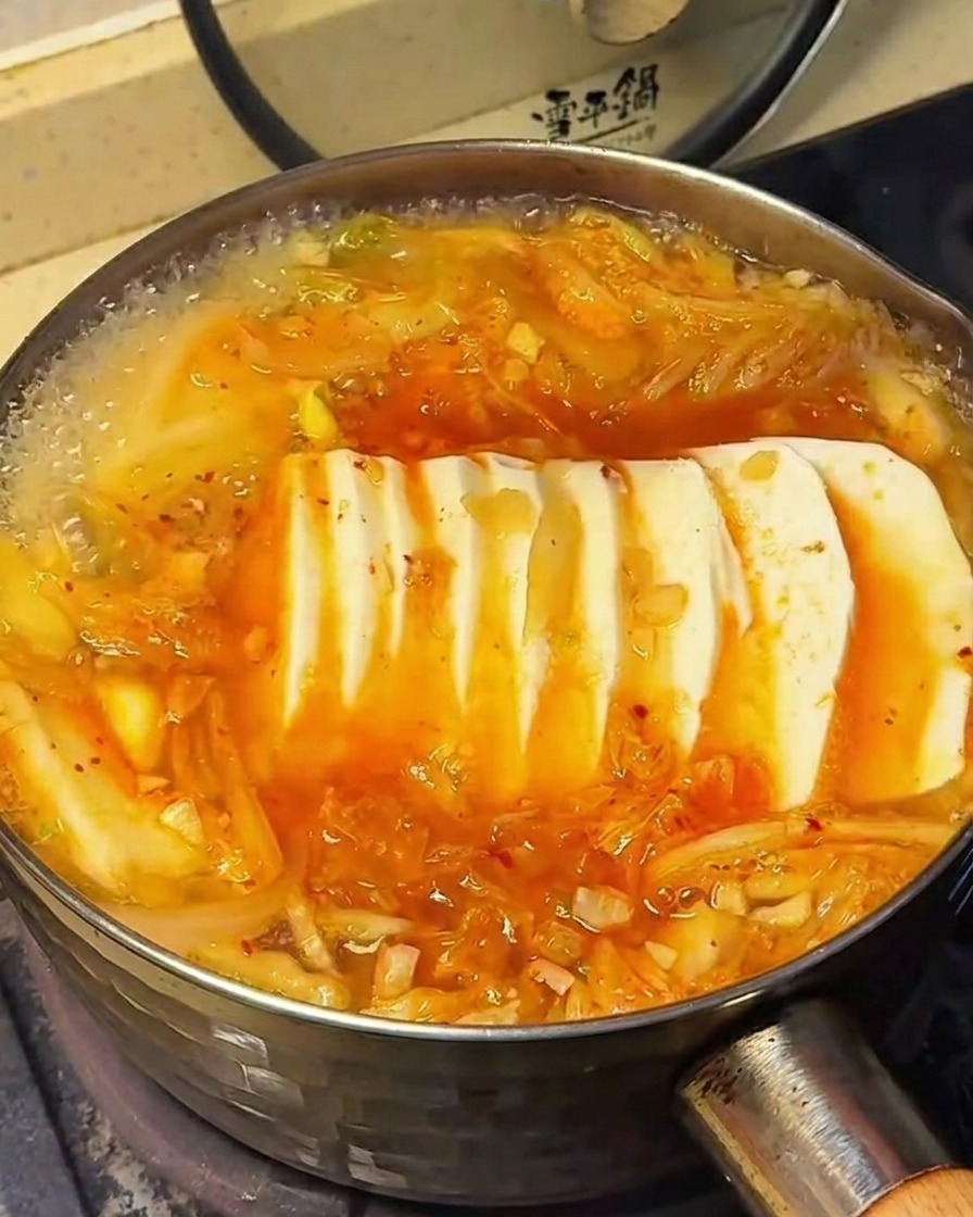 La superficie della zuppa di kimchi con tofu mentre vengono aggiunti i condimenti.