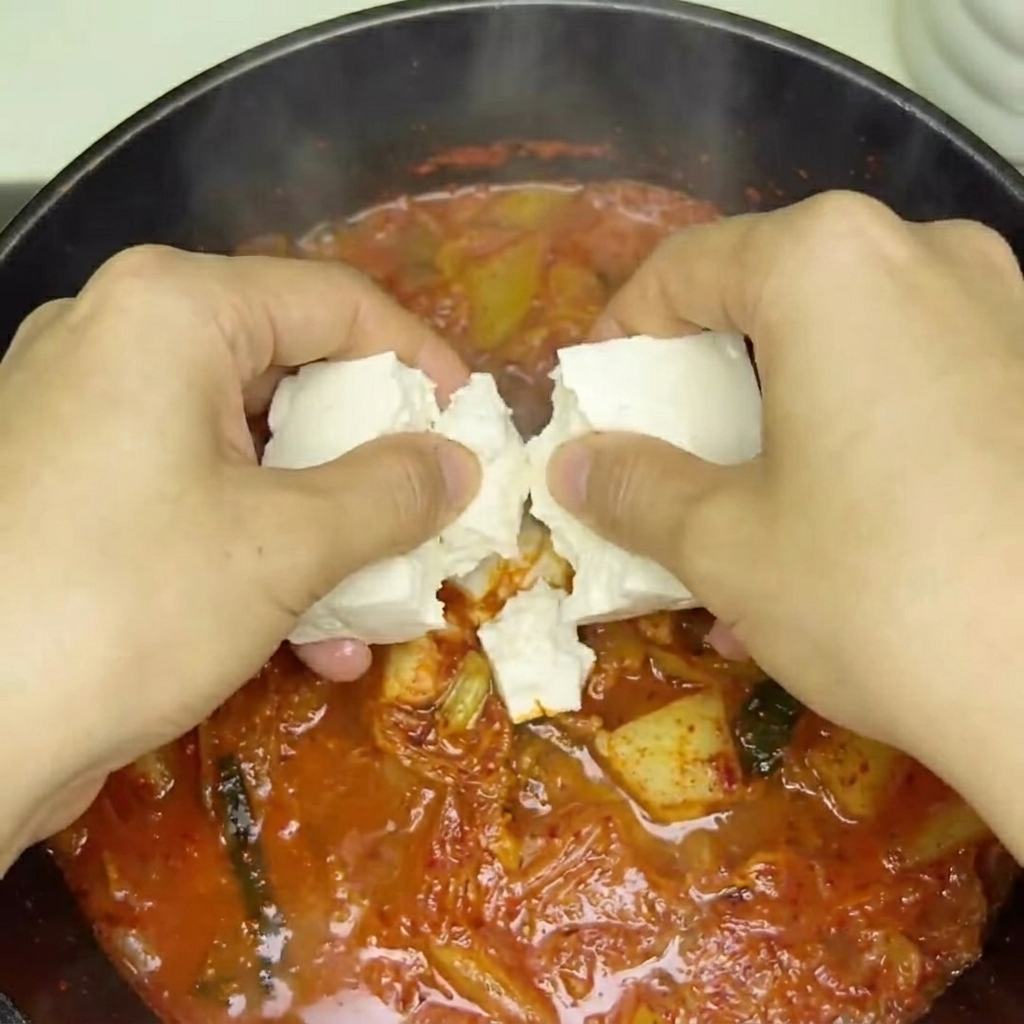 Cubetti di tofu fresco inseriti nella zuppa di kimchi in ebollizione.