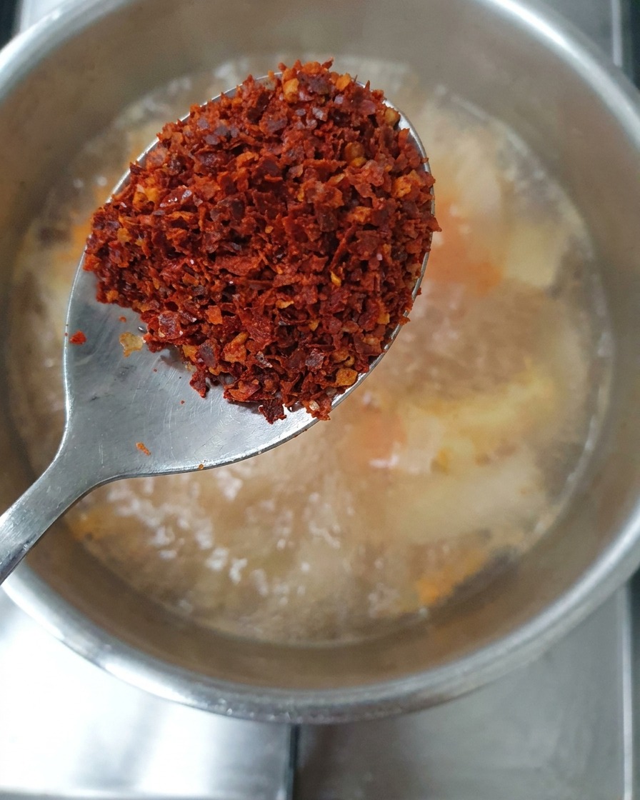 Un cucchiaio contenente un mix di fiocchi di peperoncino rossi grossolani e fini tenuto sopra lo stufato.
