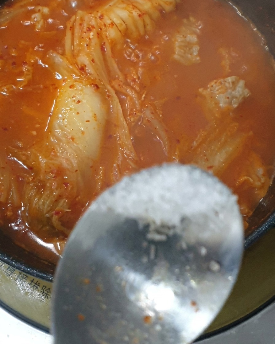 Un cucchiaio di condimento aggiunto allo stufato di kimchi rosso in ebollizione.