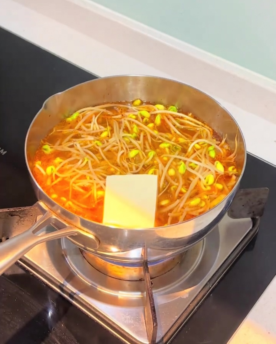 Fette di tofu bianco e torte di pesce aggiunte alla base di zuppa di kimchi arancione in ebollizione.