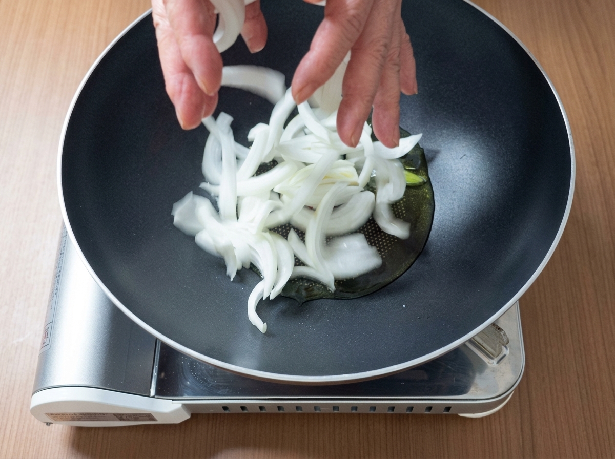 Pezzi di maiale e cipolle a fette che sfrigolano insieme in una padella con olio.