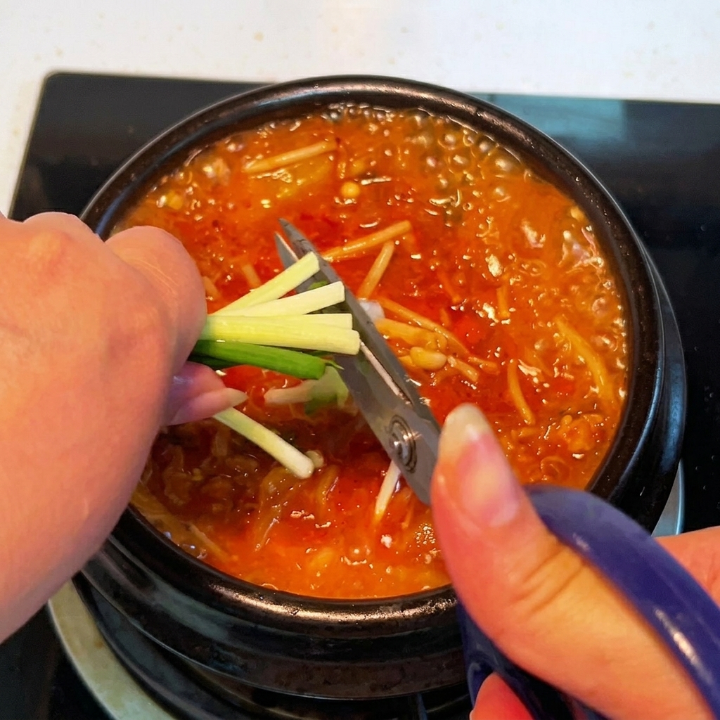 Cipollotti freschi tagliati direttamente sopra la pentola di stufato di kimchi che sobbolle usando le forbici da cucina.